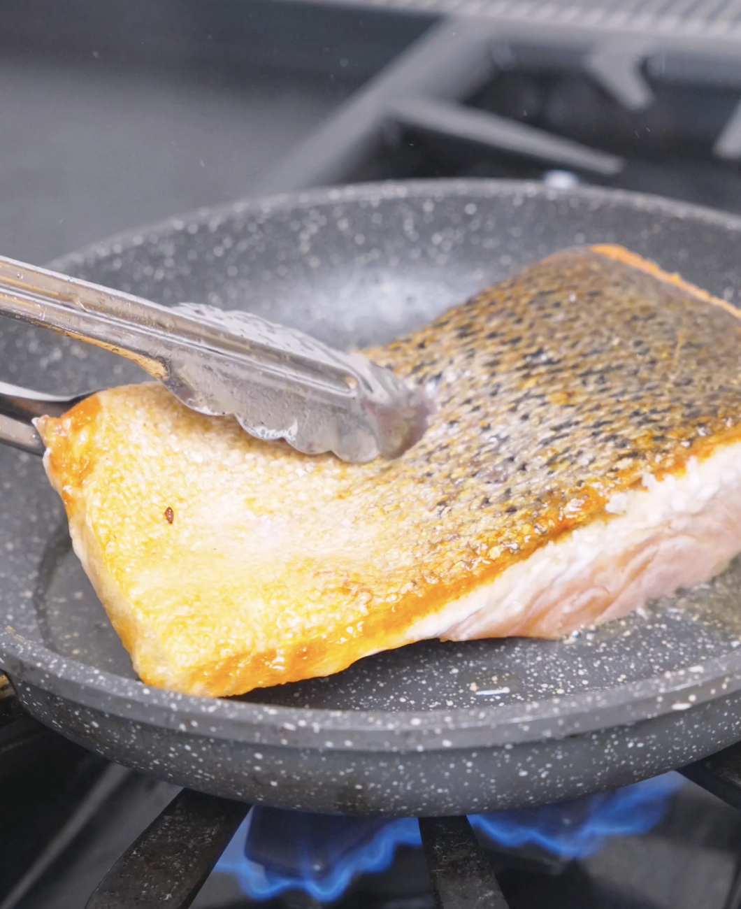 A salmon fillet searing with crisp golden edges in the pan for Spicy Salmon Bowl Recipe.