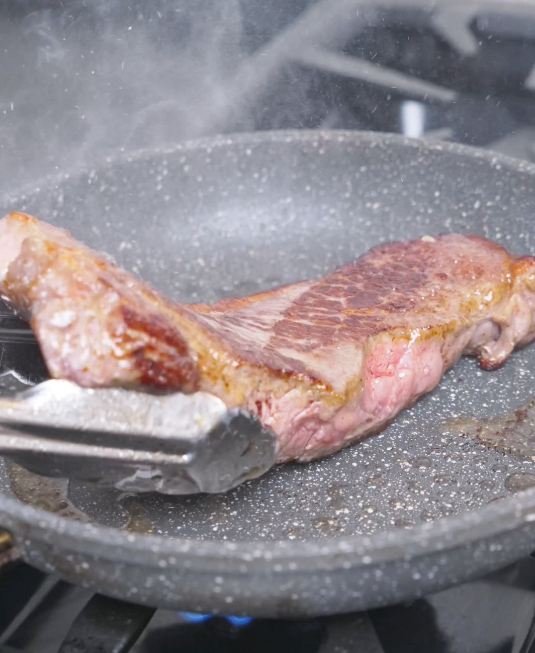 A ribeye searing in a hot pan, flipped with tongs every thirty seconds, for Japanese Steak Bowl Recipe.