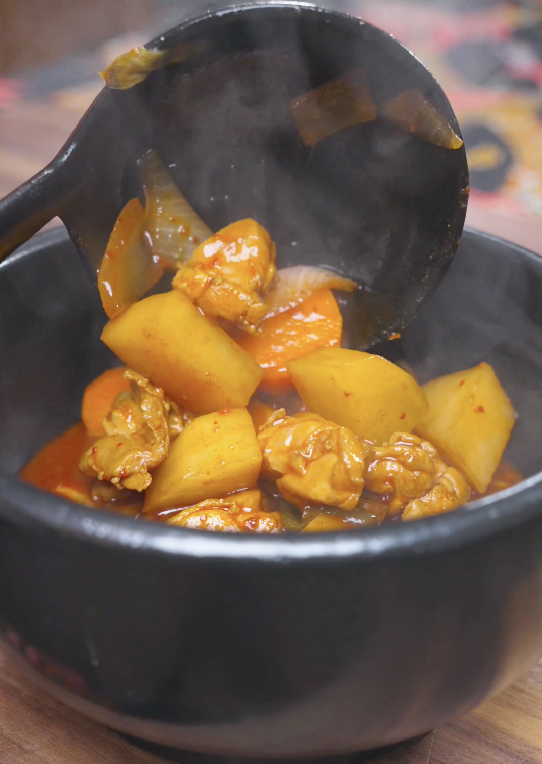 A ladle spooning steaming chicken, potatoes, and carrots into a bowl for Korean Braised Chicken Recipe.