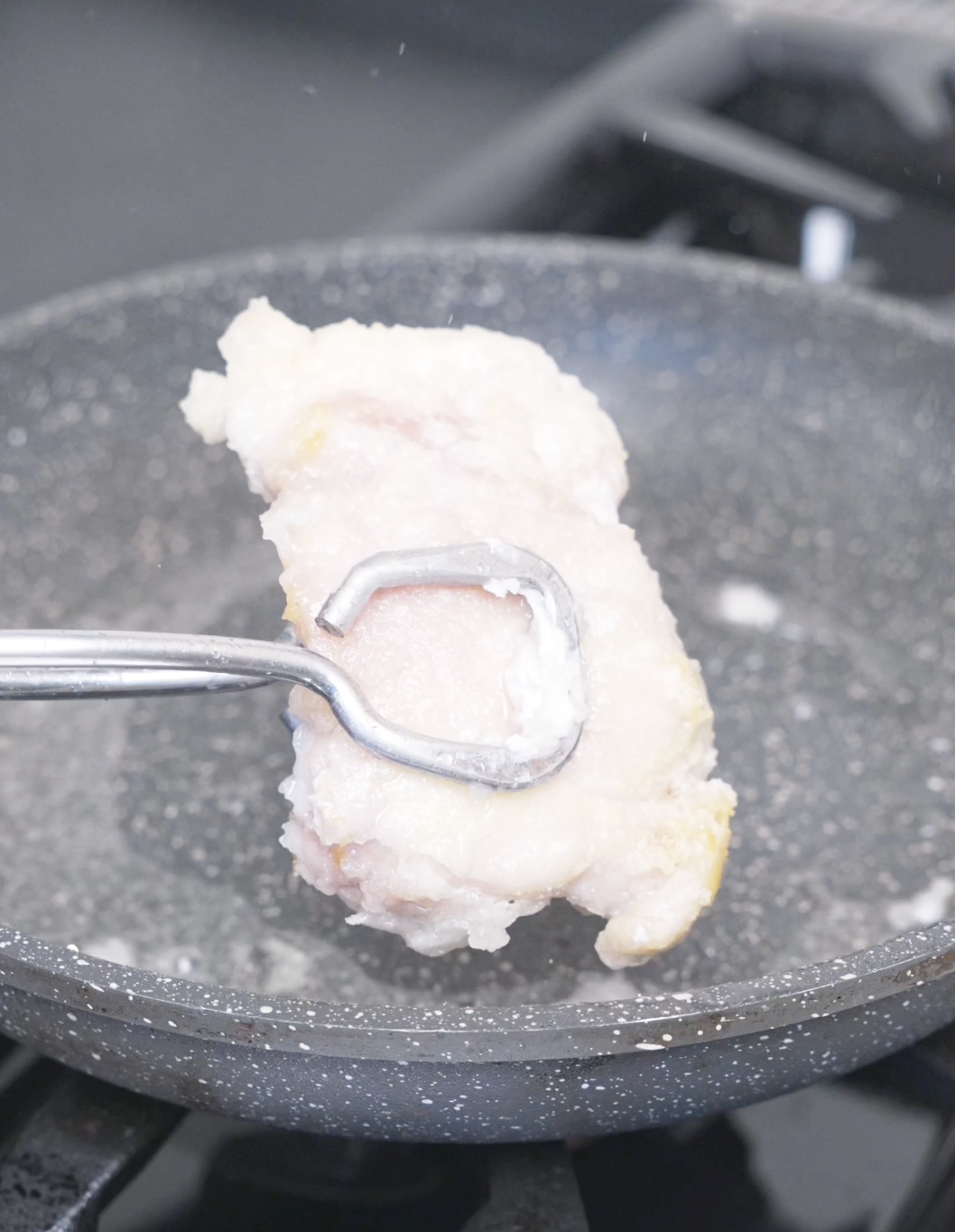 A cornstarch-coated thigh being flipped with tongs as it crisps in the pan for Creamy Gochujang Chicken Recipe.