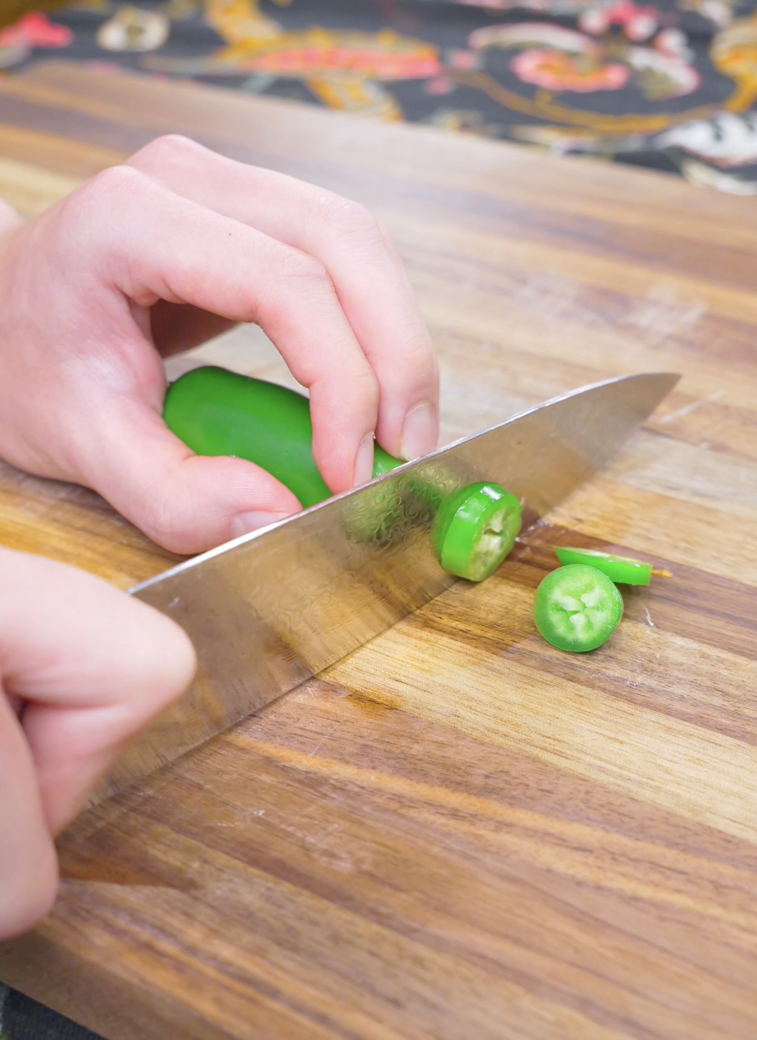 A jalape&ntilde;o being sliced into rings on a wooden board for Salt and Pepper Shrimp Recipe.