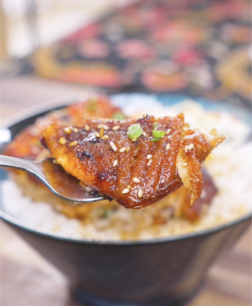 A spoon lifting a flake of glazed salmon with sesame seeds and scallions above the bowl of Spicy Salmon Bowl Recipe.