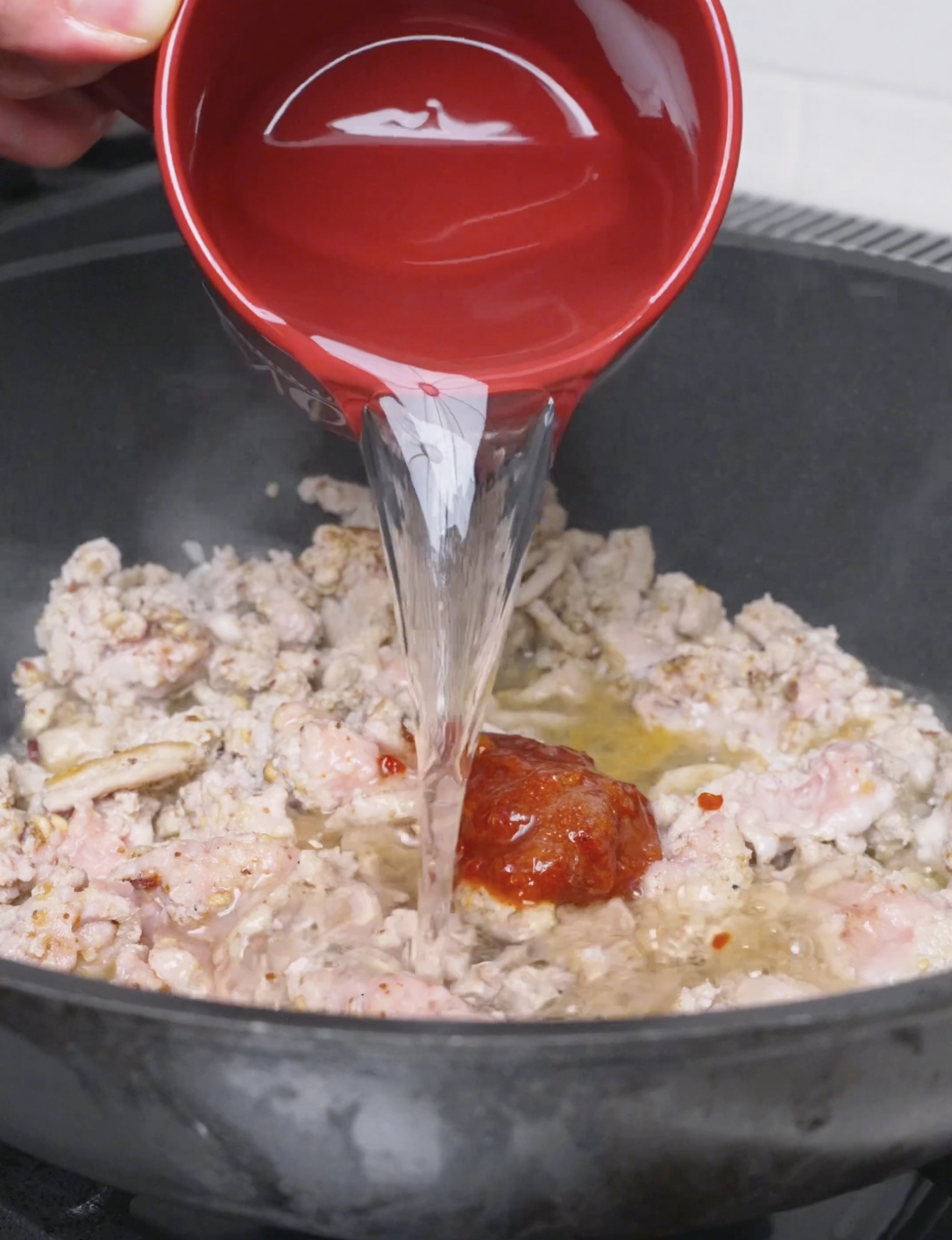 Water being poured in over a spoonful of spicy bean paste for Mapo Tofu Recipe.