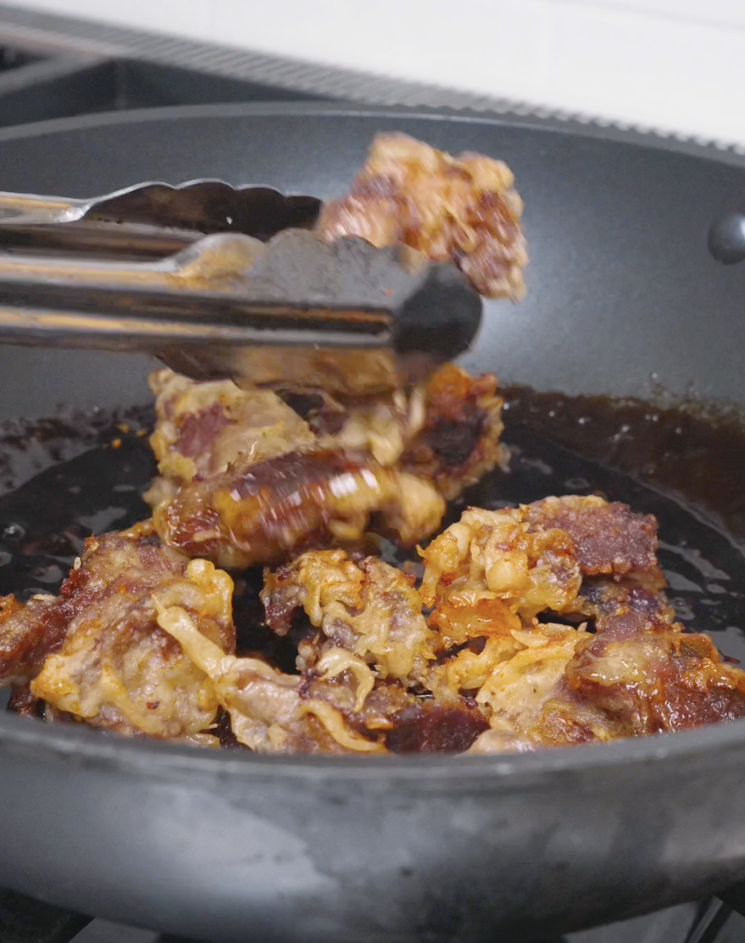 Crispy fried beef being returned to the pan of thickened sauce for Orange Beef Recipe.
