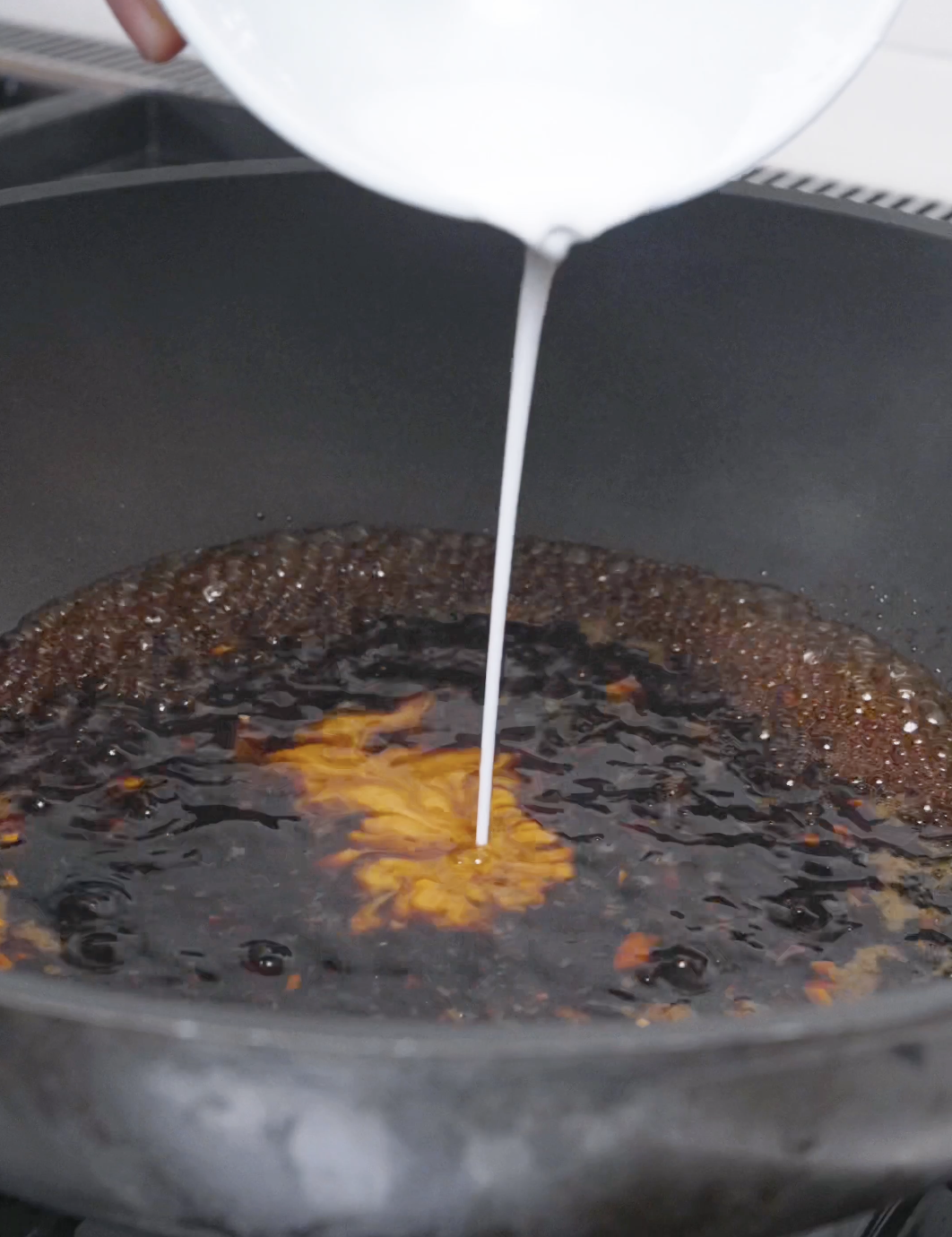 A cornstarch slurry being poured into the simmering citrus sauce for Orange Beef Recipe.