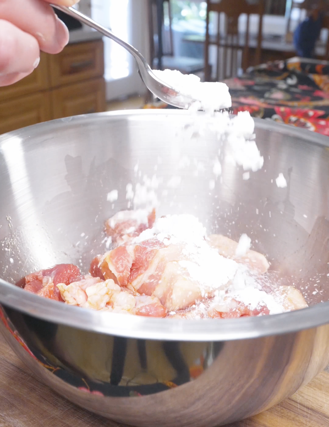 Cornstarch being sprinkled over the seasoned pork belly cubes for Deep Fried Pork Belly Recipe.