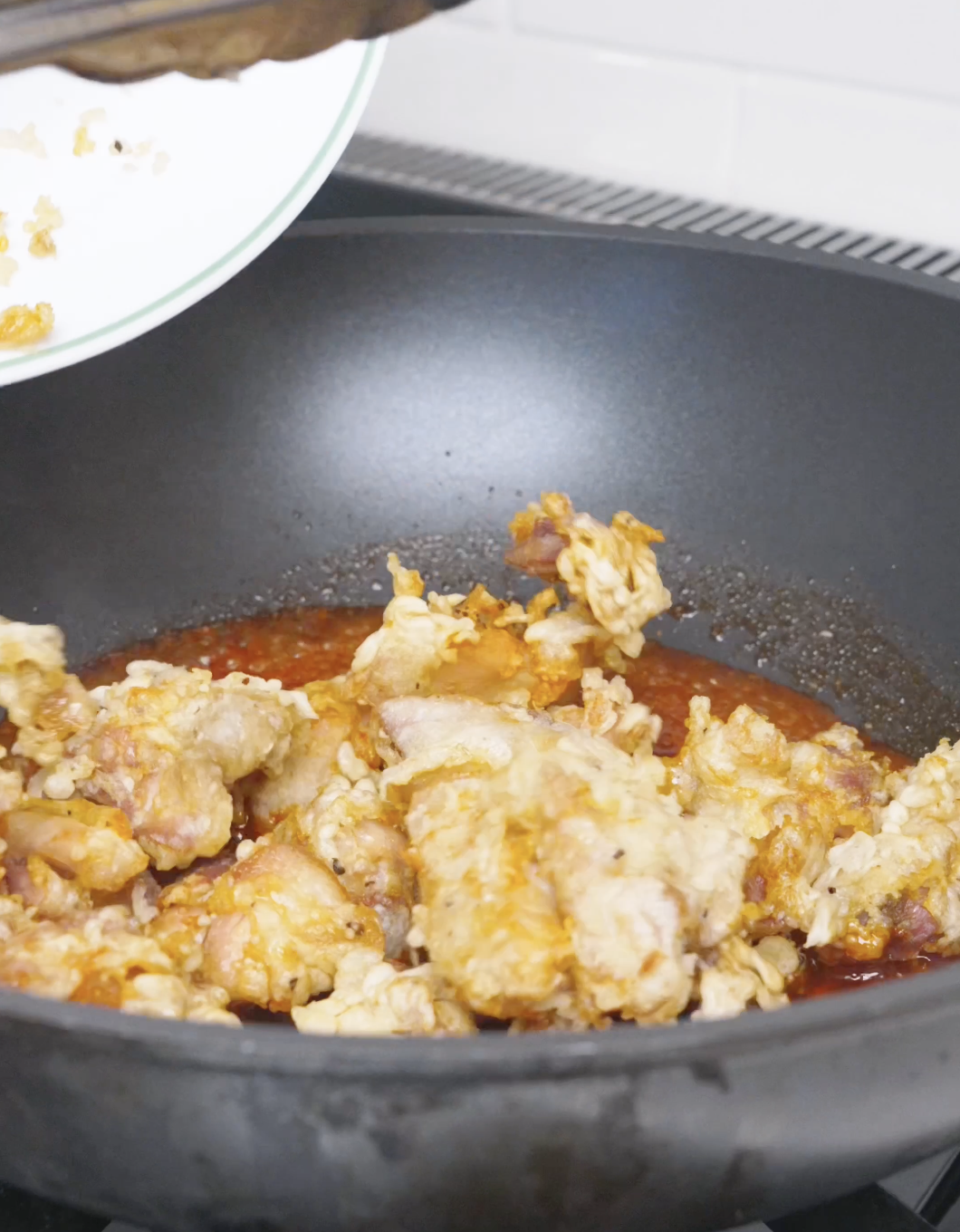 Crispy fried chicken being tipped into the simmering sauce for Korean Popcorn Chicken Recipe.