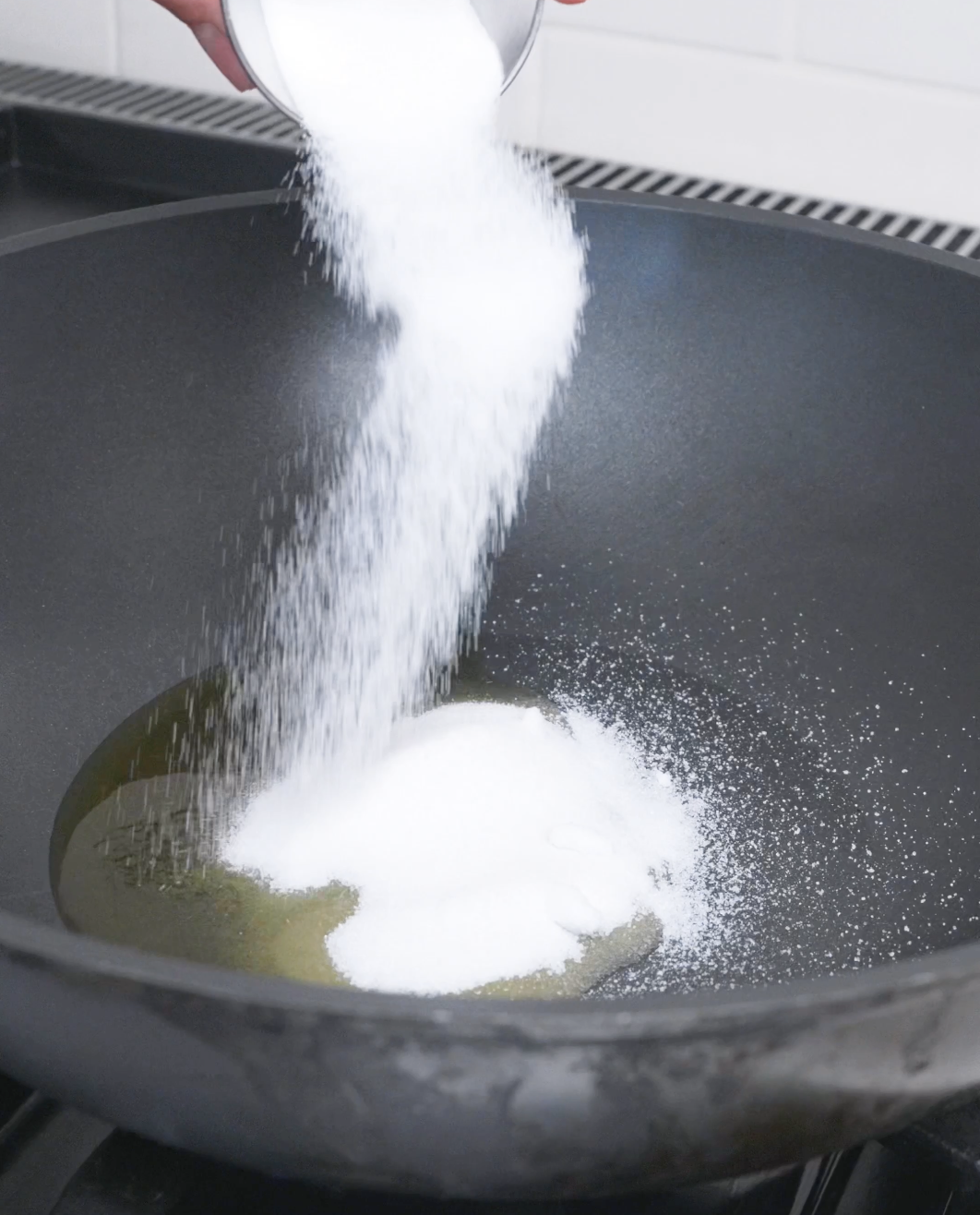 Sugar being poured into an oiled wok to begin the caramel for Red Braised Pork Belly Recipe.