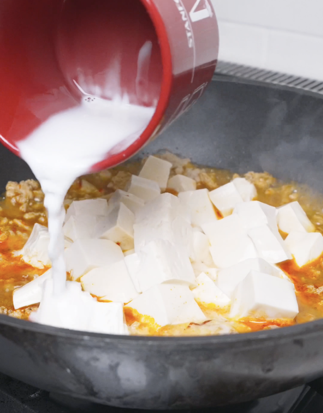 A cornstarch slurry being poured over the tofu chunks in the simmering sauce for Mapo Tofu Recipe.