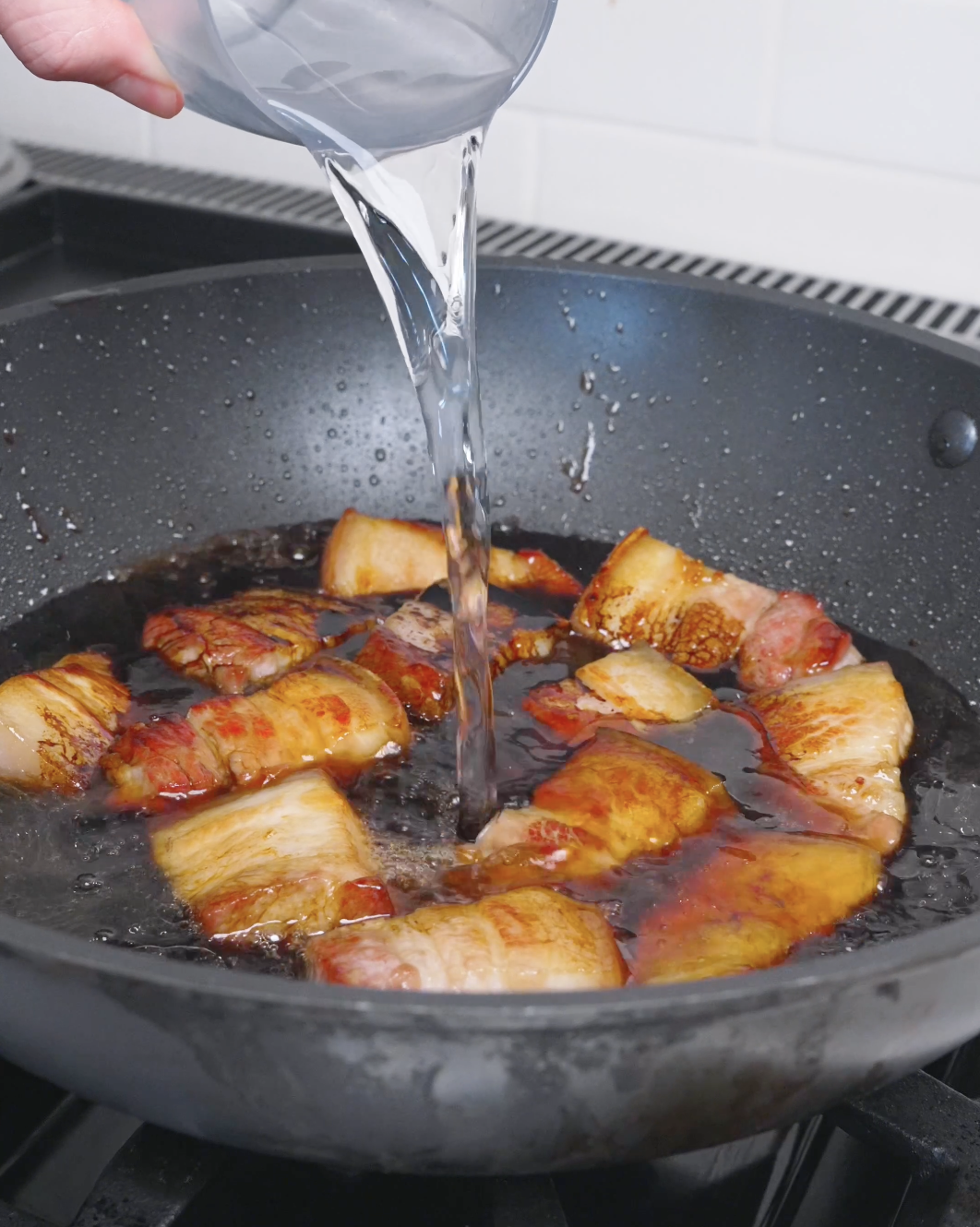 Water being poured over the browned pork and soy sauce to cover it for Red Braised Pork Belly Recipe.