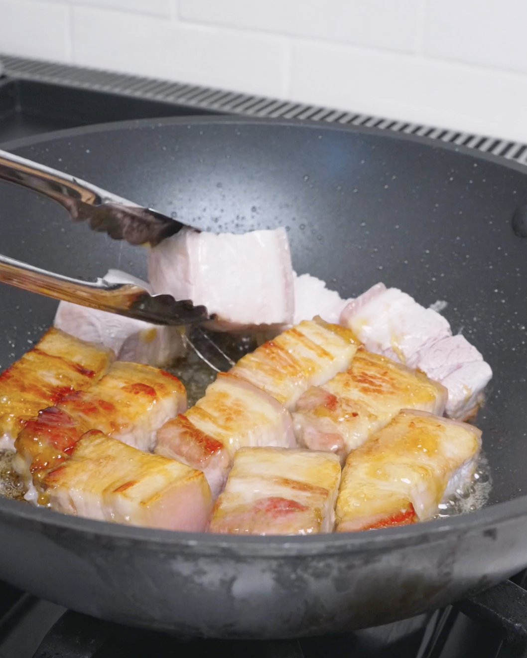 Blanched pork belly being turned with tongs to brown on all sides for Red Braised Pork Belly Recipe.