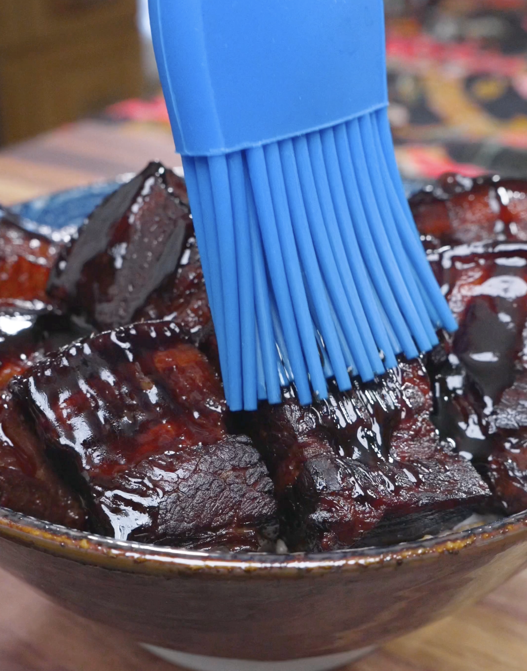 A silicone brush spreading extra glossy sauce over the plated pork for Red Braised Pork Belly Recipe.