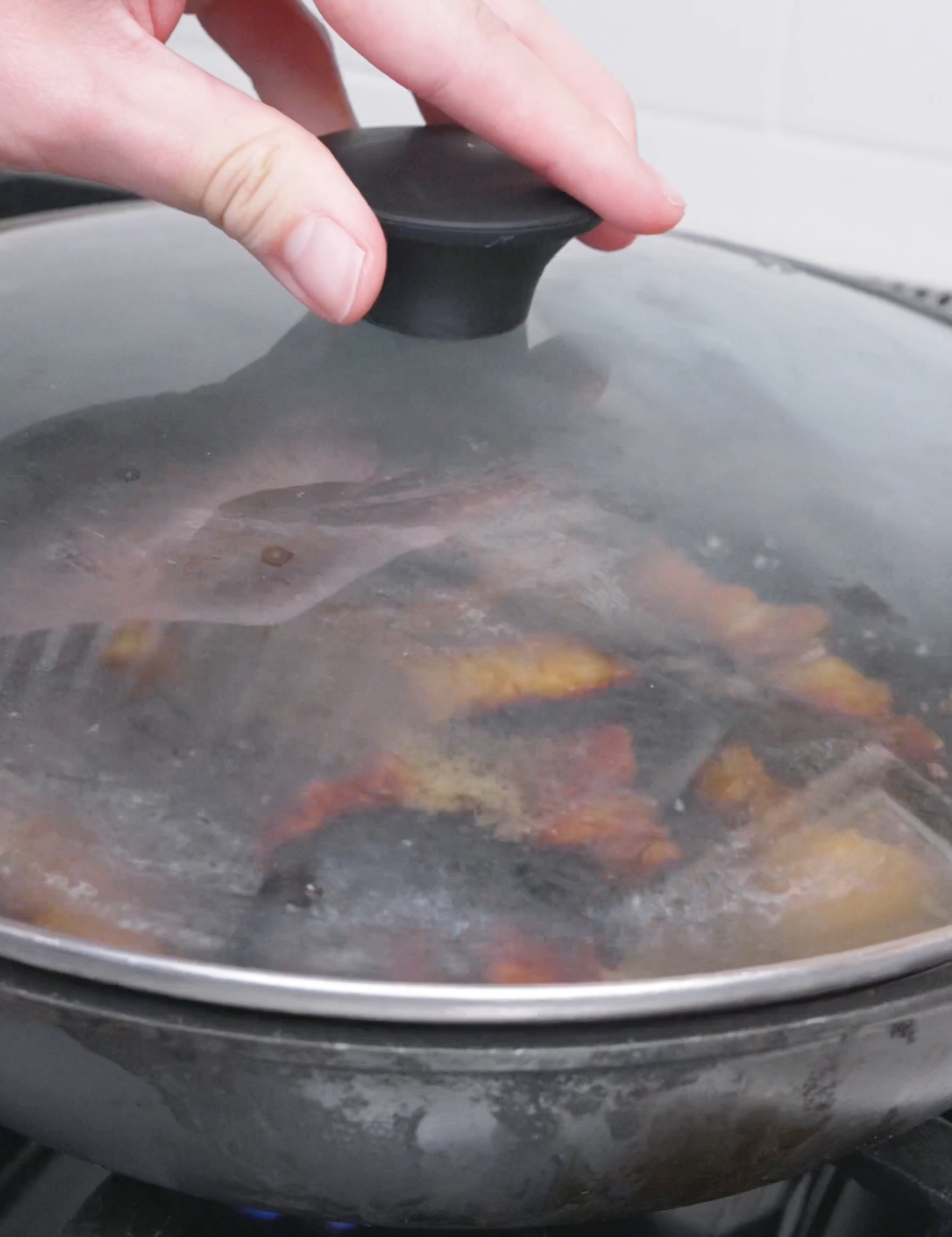 A glass lid being set over the simmering pan to braise for an hour for Red Braised Pork Belly Recipe.