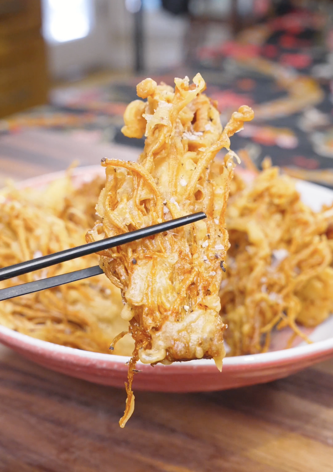 A single shattering-crisp cluster held up above the plate of Crispy Fried Enoki Mushrooms Recipe.
