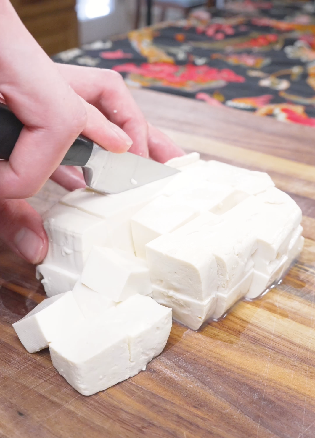 A block of silken tofu being cut into rough chunks on a wooden board for Mapo Tofu Recipe.
