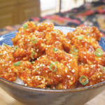 Finished Korean Popcorn Chicken Recipe over rice with sesame seeds and sliced scallions.