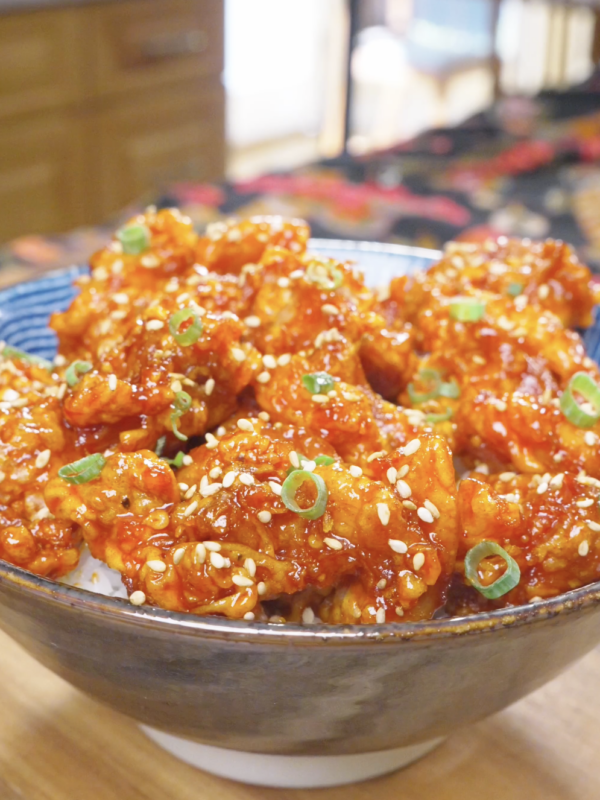 Finished Korean Popcorn Chicken Recipe over rice with sesame seeds and sliced scallions.
