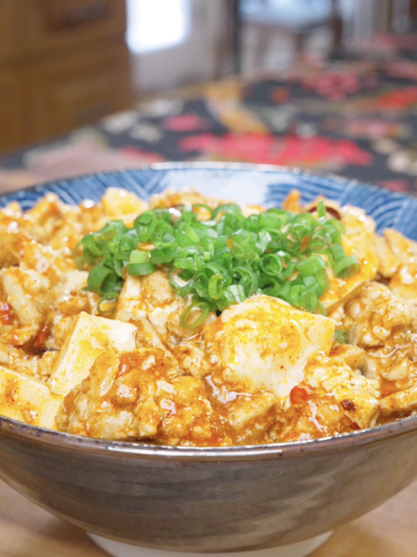 Finished Mapo Tofu Recipe in a blue bowl with silken tofu in red sauce and scallions.