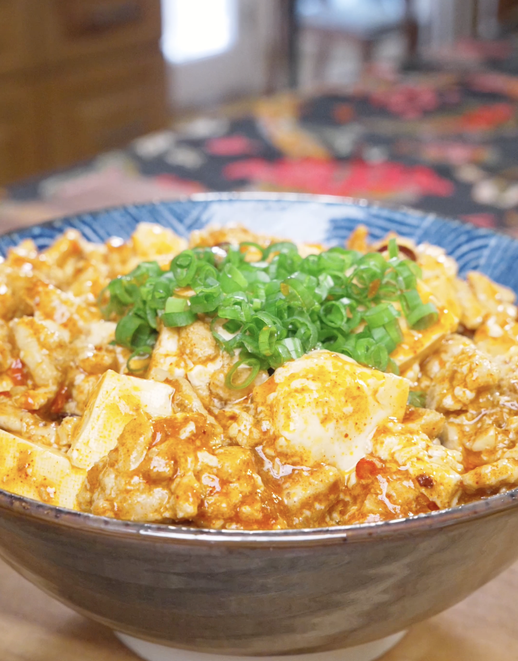 Finished Mapo Tofu Recipe in a blue bowl with silken tofu in red sauce and scallions.