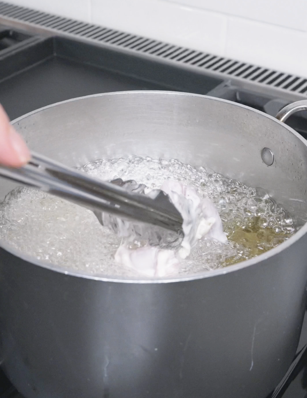 Battered chicken being lowered into bubbling oil with tongs for Korean Popcorn Chicken Recipe.