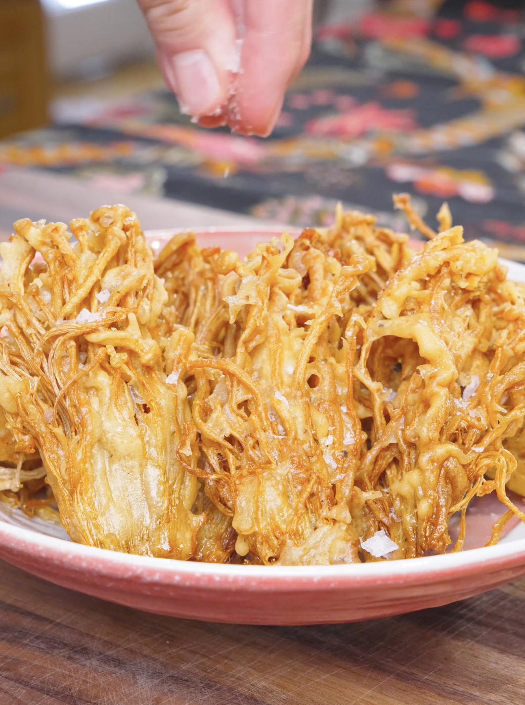 Flaky salt being sprinkled over the plated clusters of Crispy Fried Enoki Mushrooms Recipe.