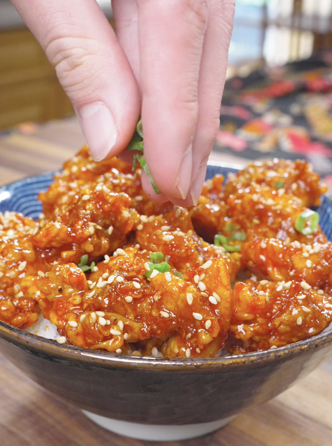 Sliced scallions being sprinkled over sesame-topped glazed chicken for Korean Popcorn Chicken Recipe.