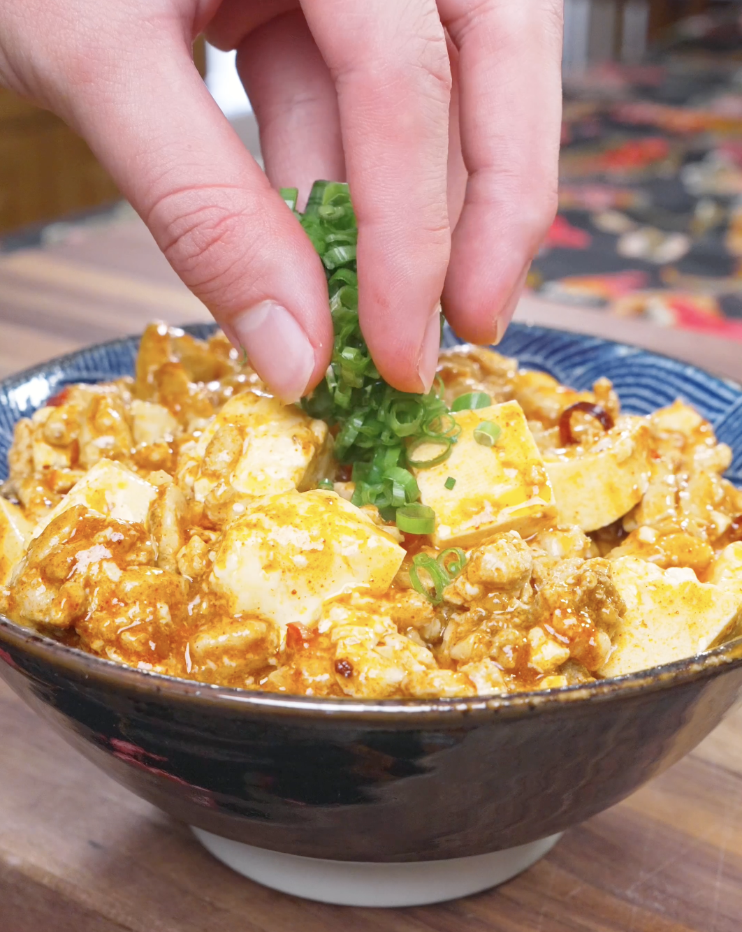 Sliced scallions being sprinkled over a bowl of Mapo Tofu Recipe.