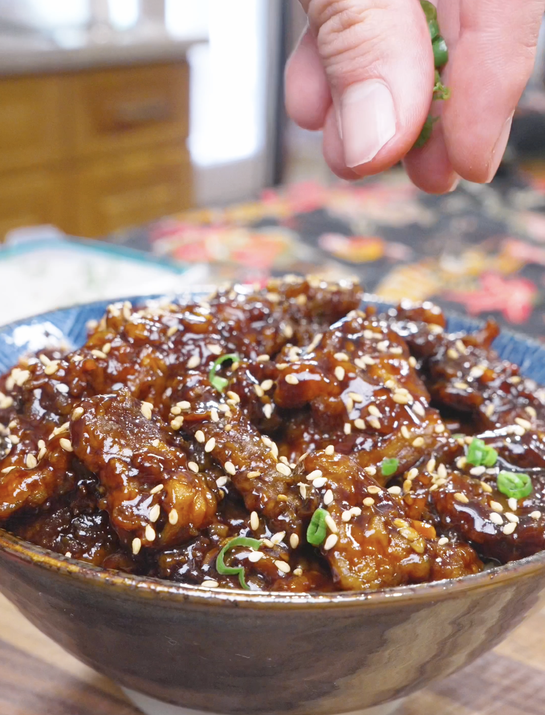 Sliced scallions being sprinkled over sesame-topped glazed beef for Orange Beef Recipe.