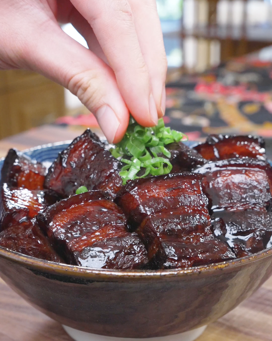 Sliced scallions being sprinkled over the lacquered pork belly for Red Braised Pork Belly Recipe.
