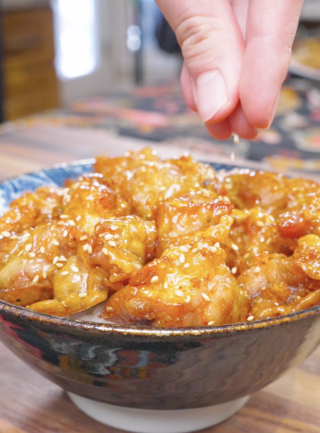Sesame seeds being sprinkled over the glazed chicken in the bowl for Sweet Honey Fried Chicken Recipe.