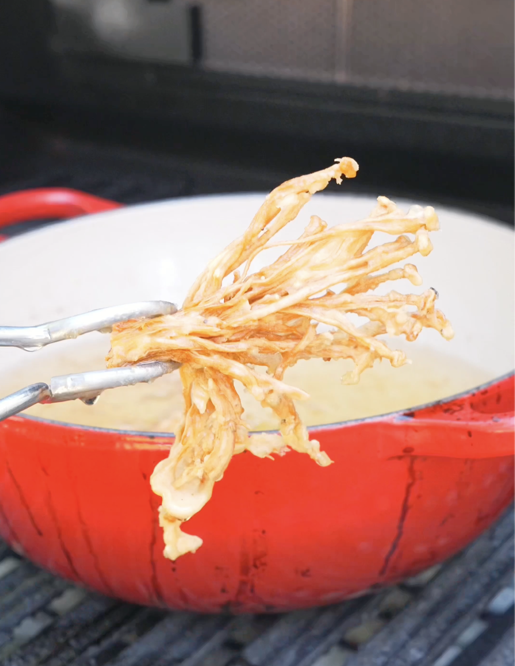 A shaggy golden-brown cluster being lifted from the oil for Crispy Fried Enoki Mushrooms Recipe.