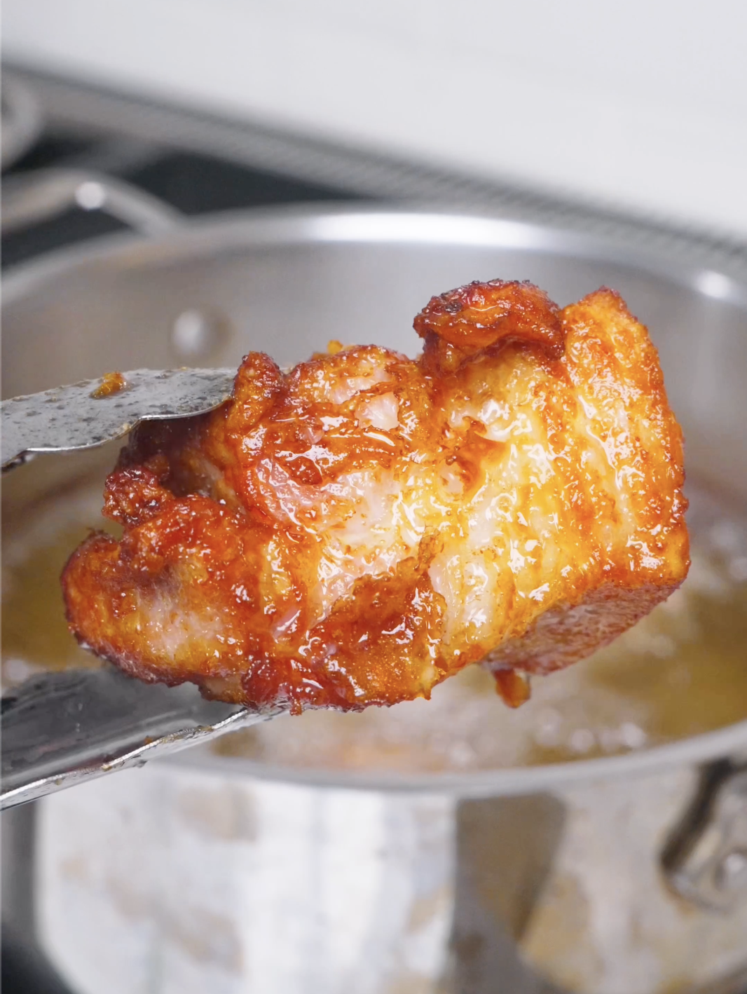 A deep caramel-brown cube being lifted from the oil for Deep Fried Pork Belly Recipe.