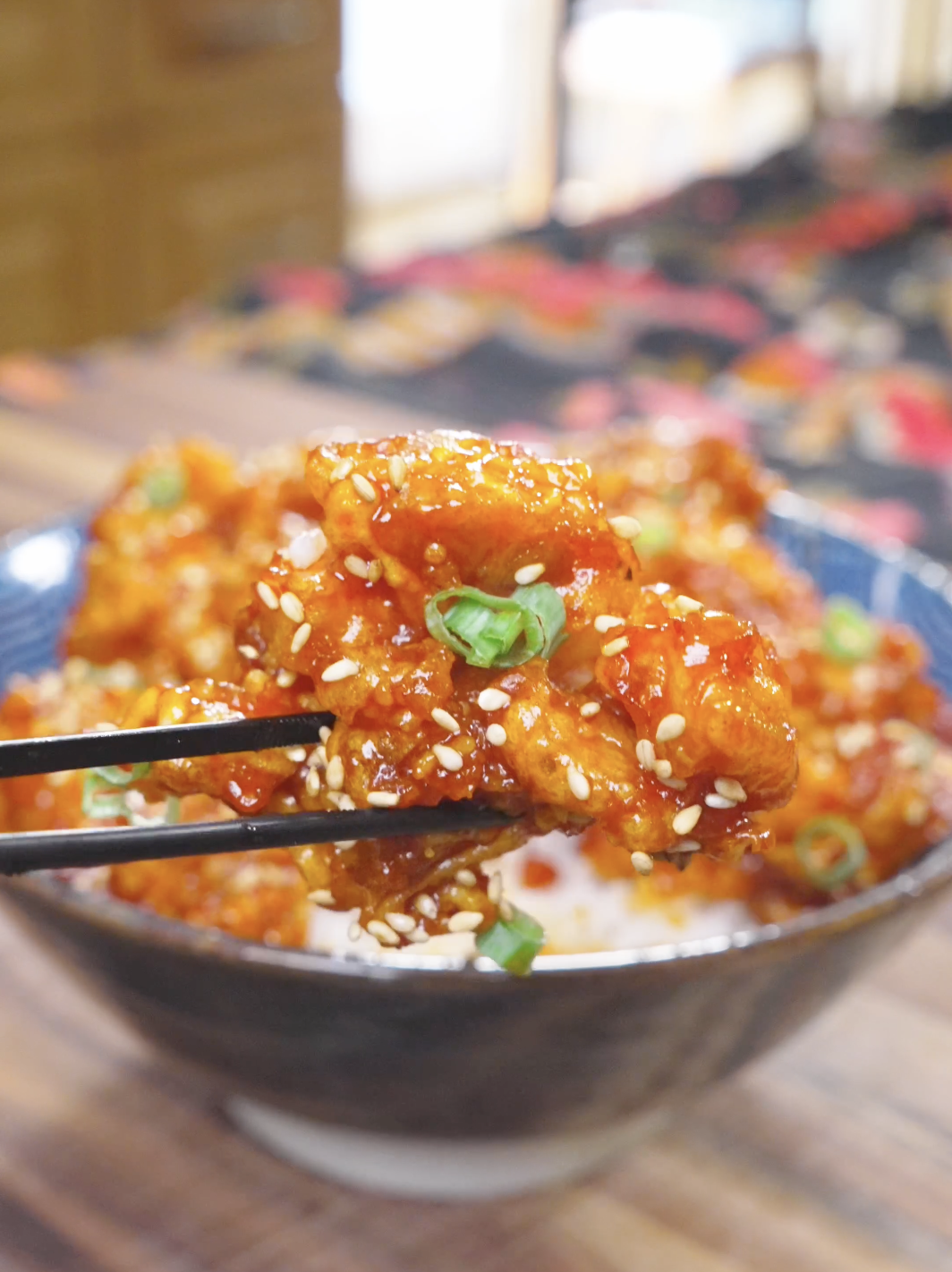 Chopsticks lifting a glossy, sesame-covered piece above the bowl of Korean Popcorn Chicken Recipe.