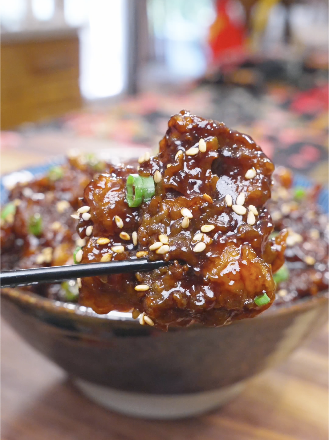 Chopsticks lifting a glossy, sesame-covered strip above the bowl of Orange Beef Recipe.
