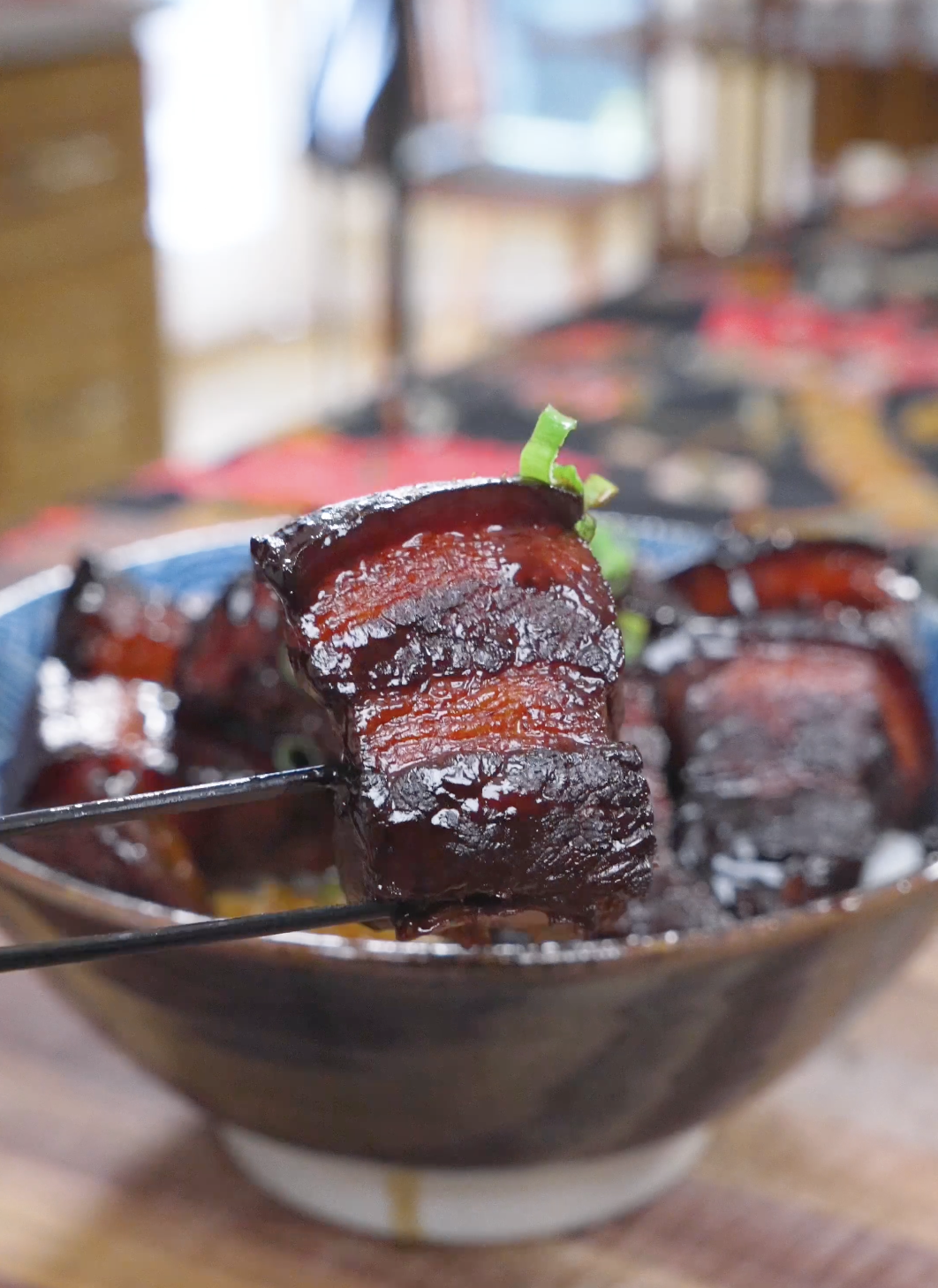 Chopsticks holding a layered, mahogany-glazed cube above the bowl of Red Braised Pork Belly Recipe.
