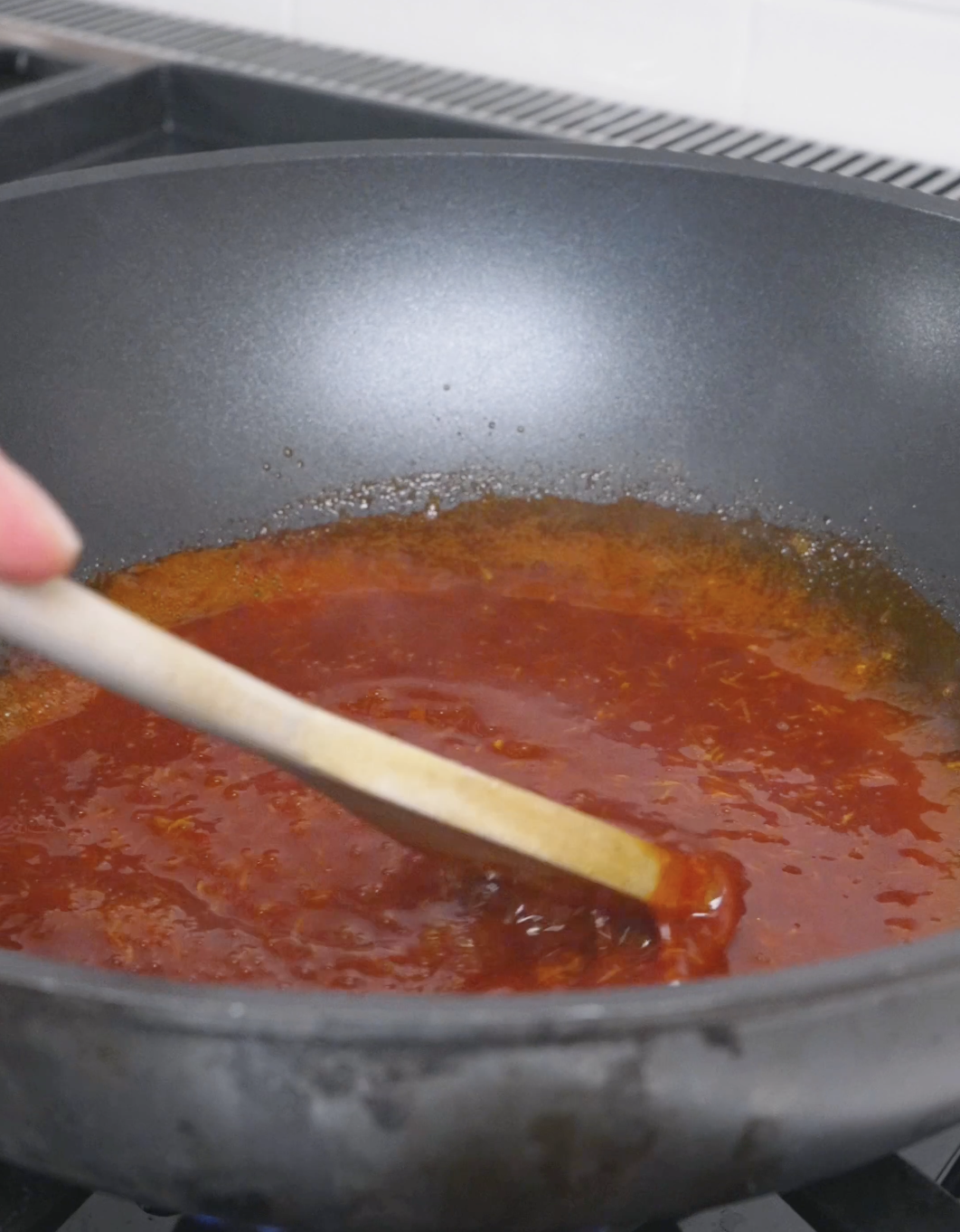 A bright red gochujang honey sauce bubbling in the pan for Korean Popcorn Chicken Recipe.