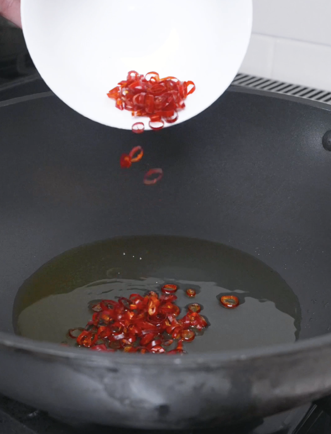 Sliced dried chilies being tipped into hot oil to toast for Mapo Tofu Recipe.